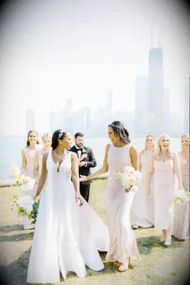 bride walks along the waterfront with chicago skyline in the background and bridesmaids wearing mismatched blush pink dresses