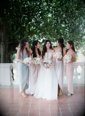 bride stands next to bridesmaids wearing mismatched pastel blue, pink and ivory floor length dresses