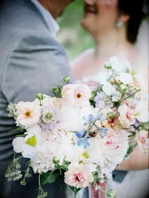 close up of bride holding pastel wedding bouquet with blue delphinium, pink cosmos, pink peonies, purple scabiosa and queen annes lace