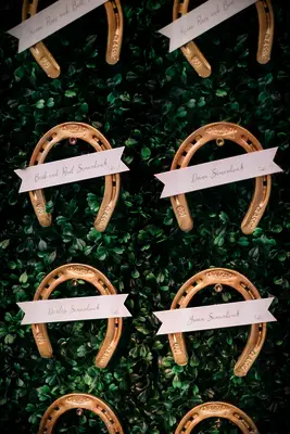 Gold horseshoe escort cards against a lush green backdrop. 