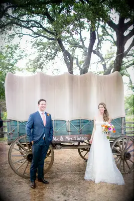 Newlyweds smile and pose in front of a covered horse carriage. 