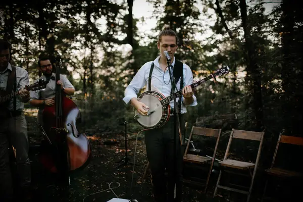Musician plays the banjo in an outdoor wooded area. 