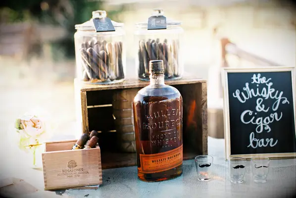 A whiskey bottle and bars of cigars sit on a table to be enjoyed by wedding guests. 