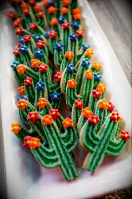 Colorful cactus-shaped cookies decorated with bright flowers and sparkling sprinkles. 