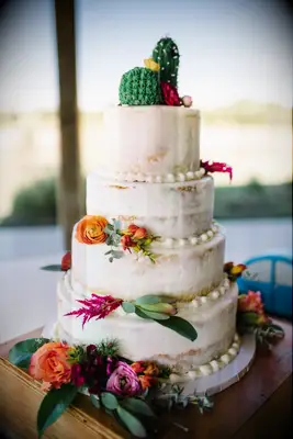 A chic three-tiered wedding cake adorned with beautiful florals and cactus-shaped decals. 