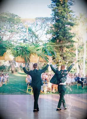 two grooms hold hands and make their entrance with sparklers at outdoor wedding reception