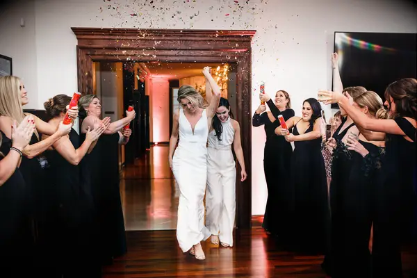 two brides hold hands while dancing into wedding reception