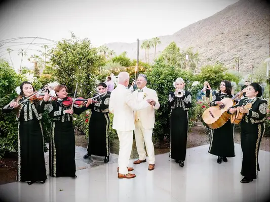 Grooms dancing to mariachi band at wedding reception