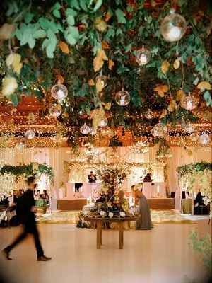 indoor wedding reception ceiling decorated with greenery, string lights and candles in floating glass orbs