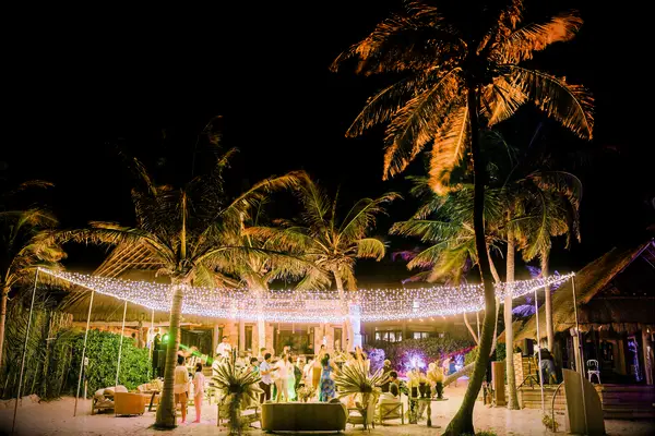 outdoor wedding reception at beach venue with a canopy of string lights hanging from palm trees above the dance floor