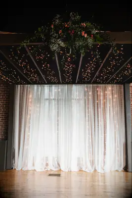 wedding ceremony backdrop with string lights showing through sheer white curtain 