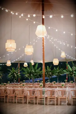 tented wedding reception with bistro string lights and mismatched rattan lanterns hanging above banquet tables