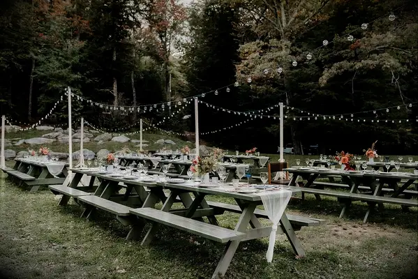 picnic tables at backyard wedding reception with bistro string lights on poles throughout the yard