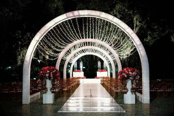 outdoor wedding ceremony at night with arched tunnel and string light canopy above the aisle