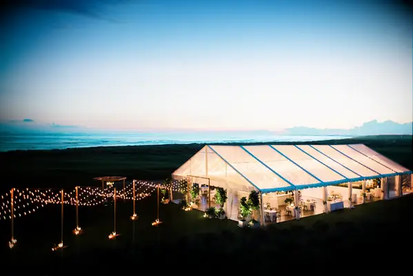 aerial view of clear top wedding reception tent at night with string lights illuminating the path to the tent