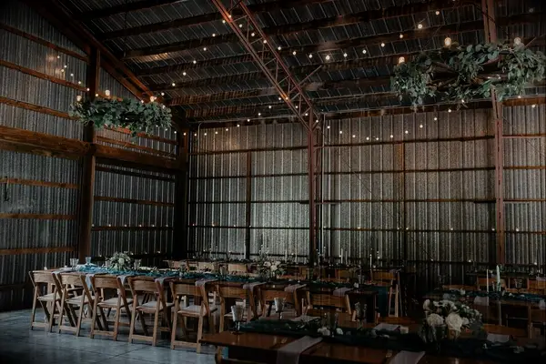 barn wedding reception venue with greenery chandeliers and bistro string lights hanging from vaulted wooden rafters