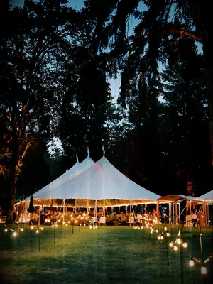 sperry wedding reception tent with bistro string lights on hooks lining the pathway across the grass