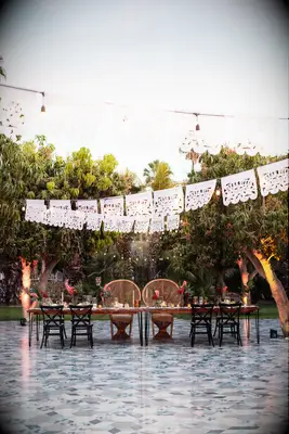 outdoor wedding reception with papel picado banners and bistro string lights hanging above colorful tile dance floor