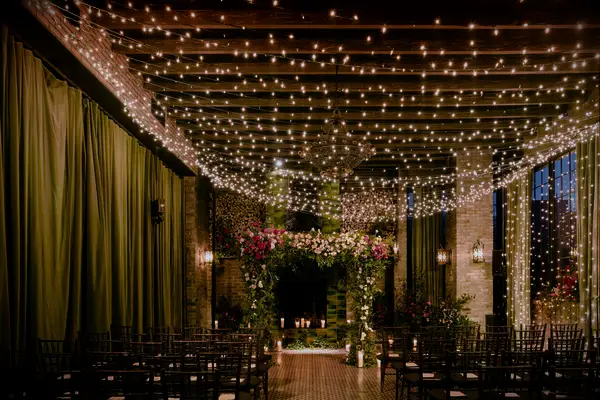 indoor wedding ceremony with flower arch at the altar beneath a canopy of string lights