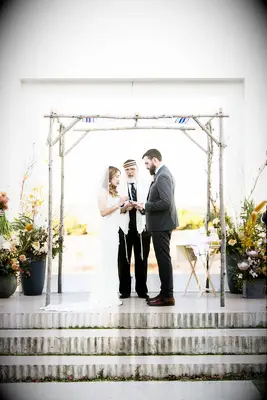 Couple exchanging rings under birch wood chuppah.