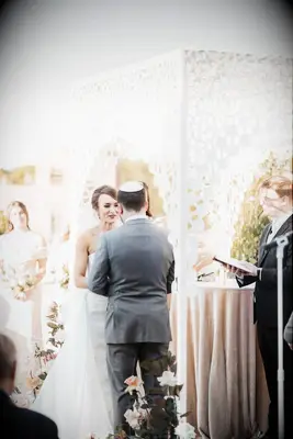Couple holding hands in front of white chuppah with laser-cut pattern.