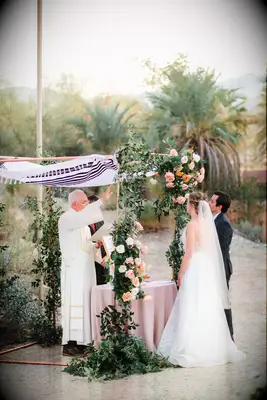 Rabbi under copper chuppah speaking to couple during desert wedding.