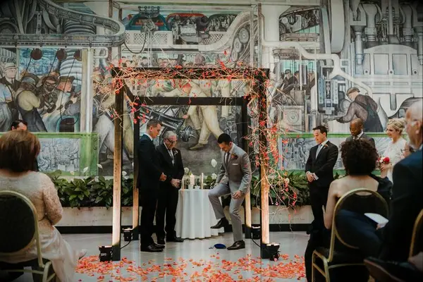 Groom breaking the glass under wood chuppah decorated with orange flowers. 