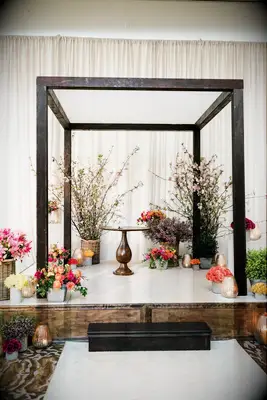 Black chuppah decorated with groupings of floral arrangements. 
