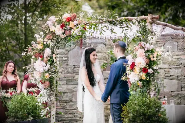Couple holding hands under birch chuppah with dahlia accents.