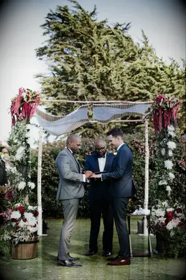 Grooms exchanging rings under birch wood chuppah. 