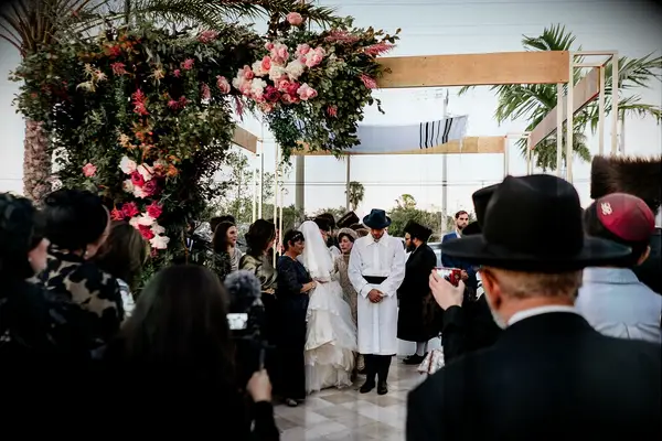 Couple and wedding guests huddled together under chuppah.