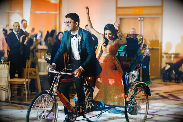 Groom carries bride in a colorful rickshaw.