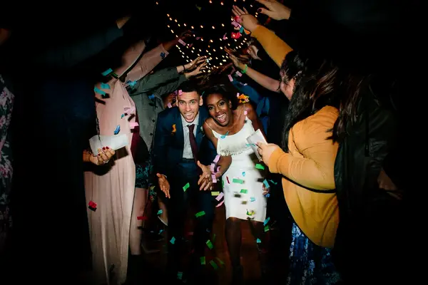 Bride and groom running under a human tunnel and confetti.