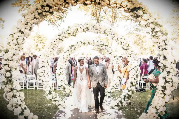Couple exiting wedding ceremony under white floral arches