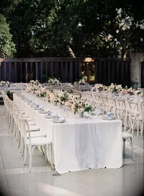 Long reception tables with white linens and white cross-back chairs