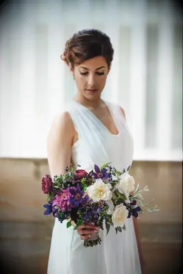bride holding small wedding bouquet with purple clematis, ivory roses, pink zinnias and red garden roses