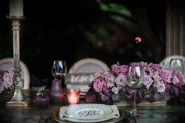 wedding tablescape with low wedding centerpiece featuring lilac and dark pink roses, votive candles and gold plates