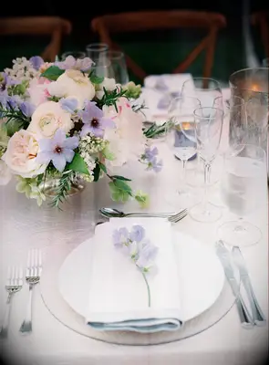 classic wedding tablescape with low centerpieces featuring purple clematis, blush garden roses and purple sweet peas on white cloth napkin at place setting