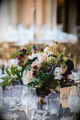 low fall wedding centerpiece with ivory roses, greenery and dark purple flowers