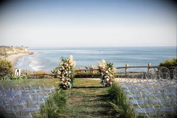 An outdoor wedding ceremony site by the ocean, with a vibrant floral arrangement at the top of the aisle.
