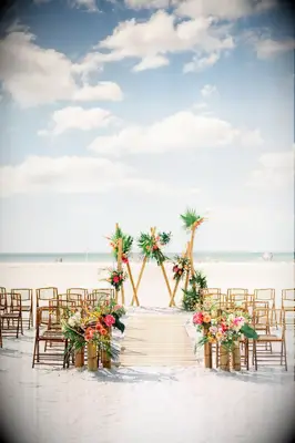 Three triangular shapes create a modern geometric wedding arch on the beach.