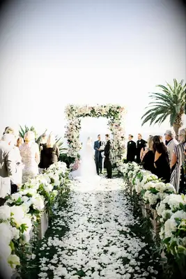 A wedding aisle lies strewn with romantic white rose petals.