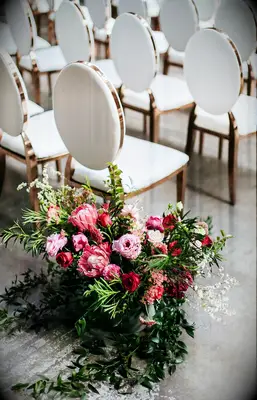 A vibrant pink floral arrangement sits beside elegant wedding chairs.