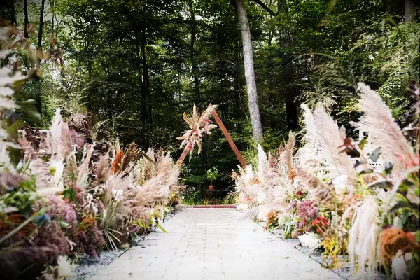Pampas grass waves guests on towards a modern geometric wedding arch.