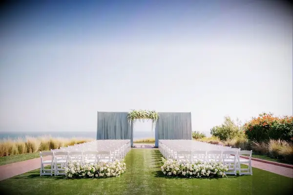 An outdoor wedding ceremony site with gorgeous white blooms and a floral archway.