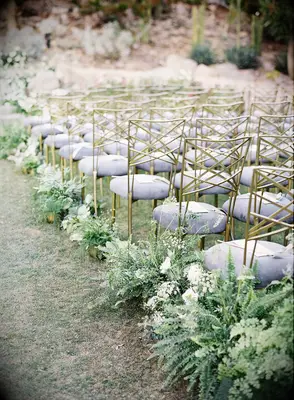 Delicate fern flower arrangements line the aisle at an outdoor wedding.