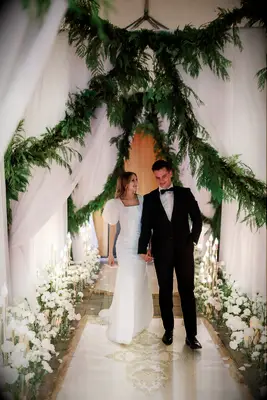Groom in Tuxedo, Bride in Puff-Sleeved Gown Walk Under Draping, Hanging Greenery Entrance