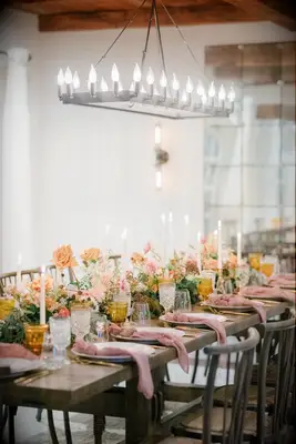 Farm table with orange flowers underneath chandelier