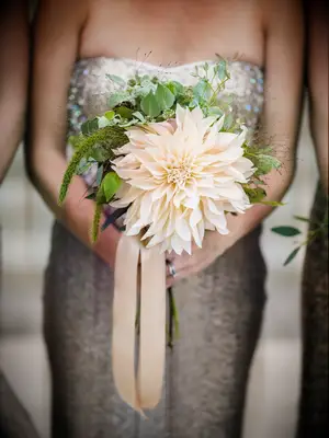 A bridesmaid holds this stunning enormous yellow flower with greenery.