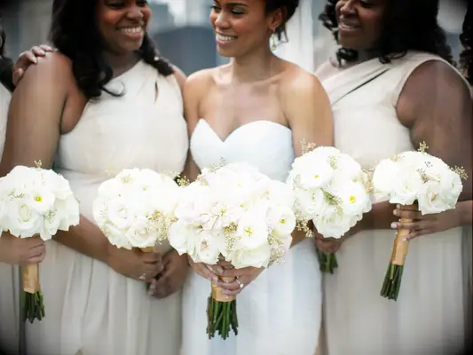A bride and her wedding party holds white rose bouquets.
